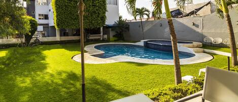 Un patio trasero con piscina, palmeras y un área de patio techada.