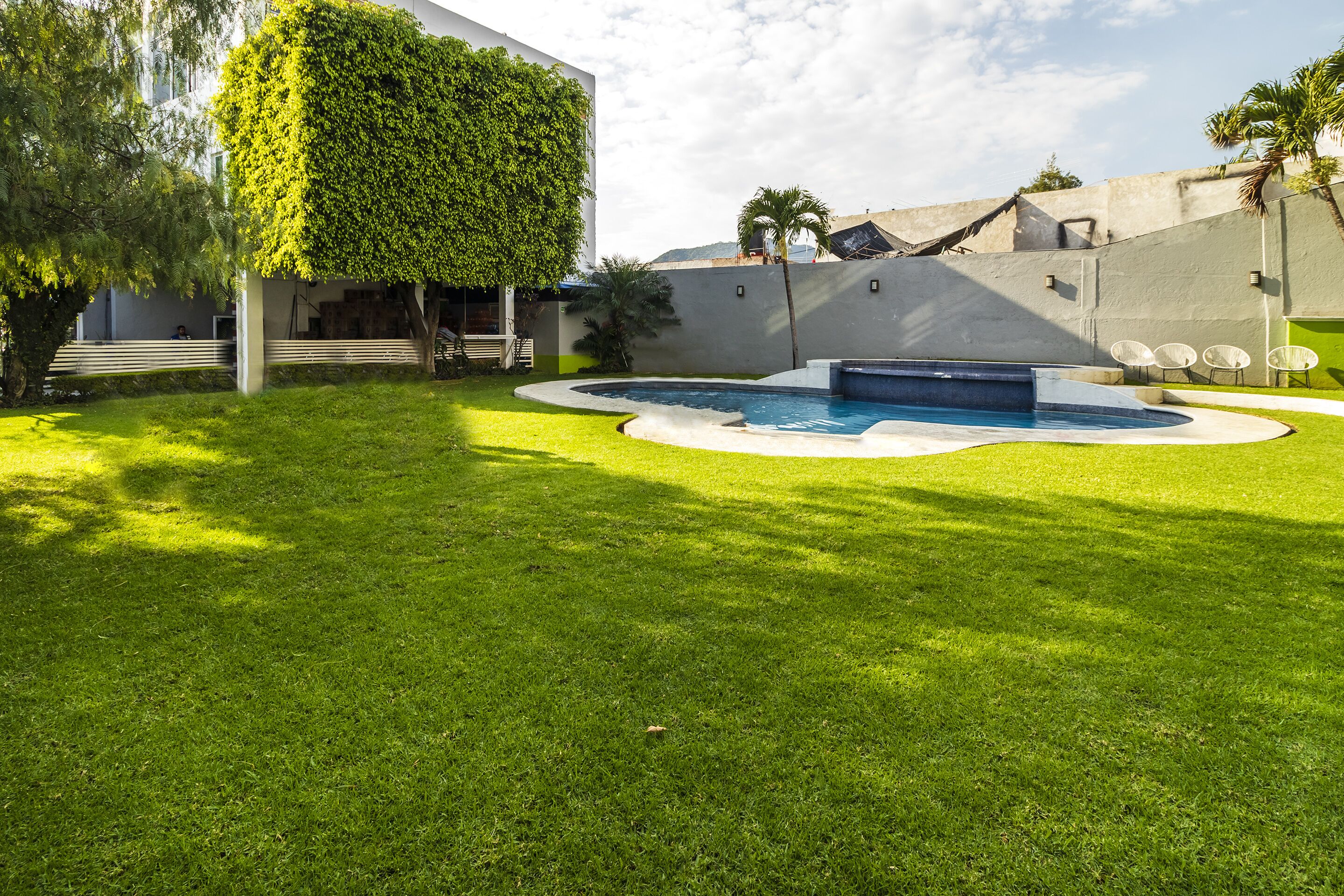 Ein moderner Poolbereich im Freien mit einem gepflegten Rasen, einem runden Pool und einem weißen Gebäude mit grüner Wand.