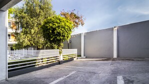 A parking area with a white fence, a tree, and a building in the background.