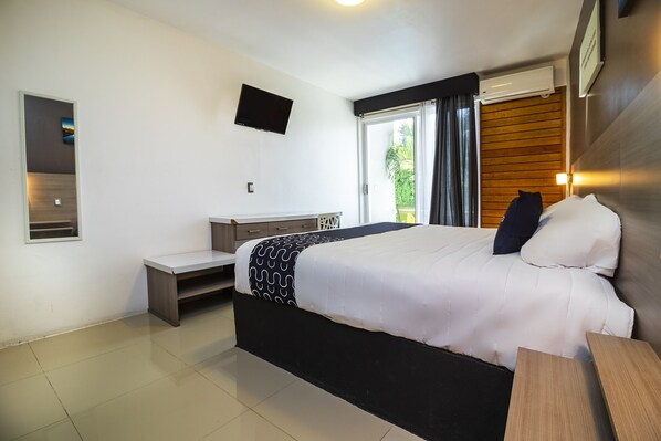 A modern hotel room with a large bed, a desk, a flat-screen TV, and a window with a view of greenery. - Collection O Hotel Mango,Six Flags Hurricane Harbor Oaxtepec (Yautepec)