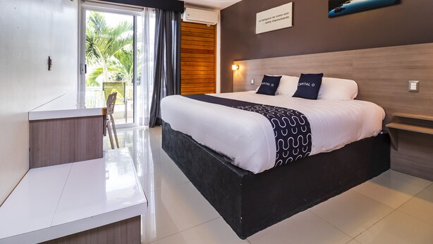 A modern hotel room with a large bed, a desk, and a view of palm trees through the window.