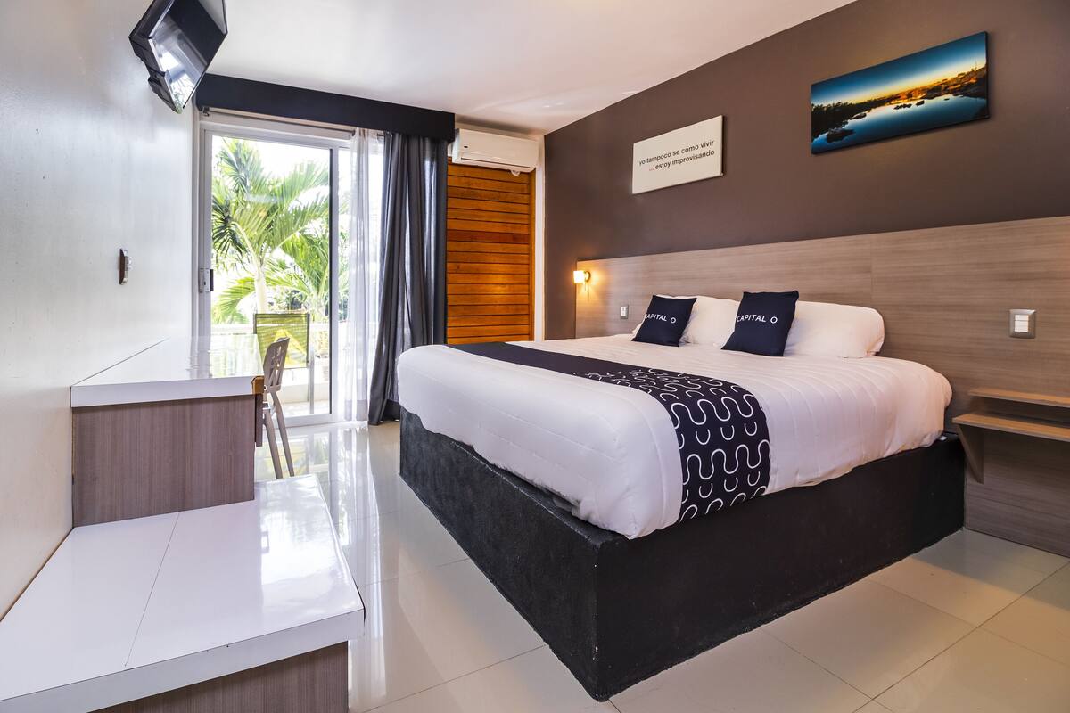 Habitación de hotel moderna con una cama grande, un escritorio y vistas a palmeras a través del ventanal.