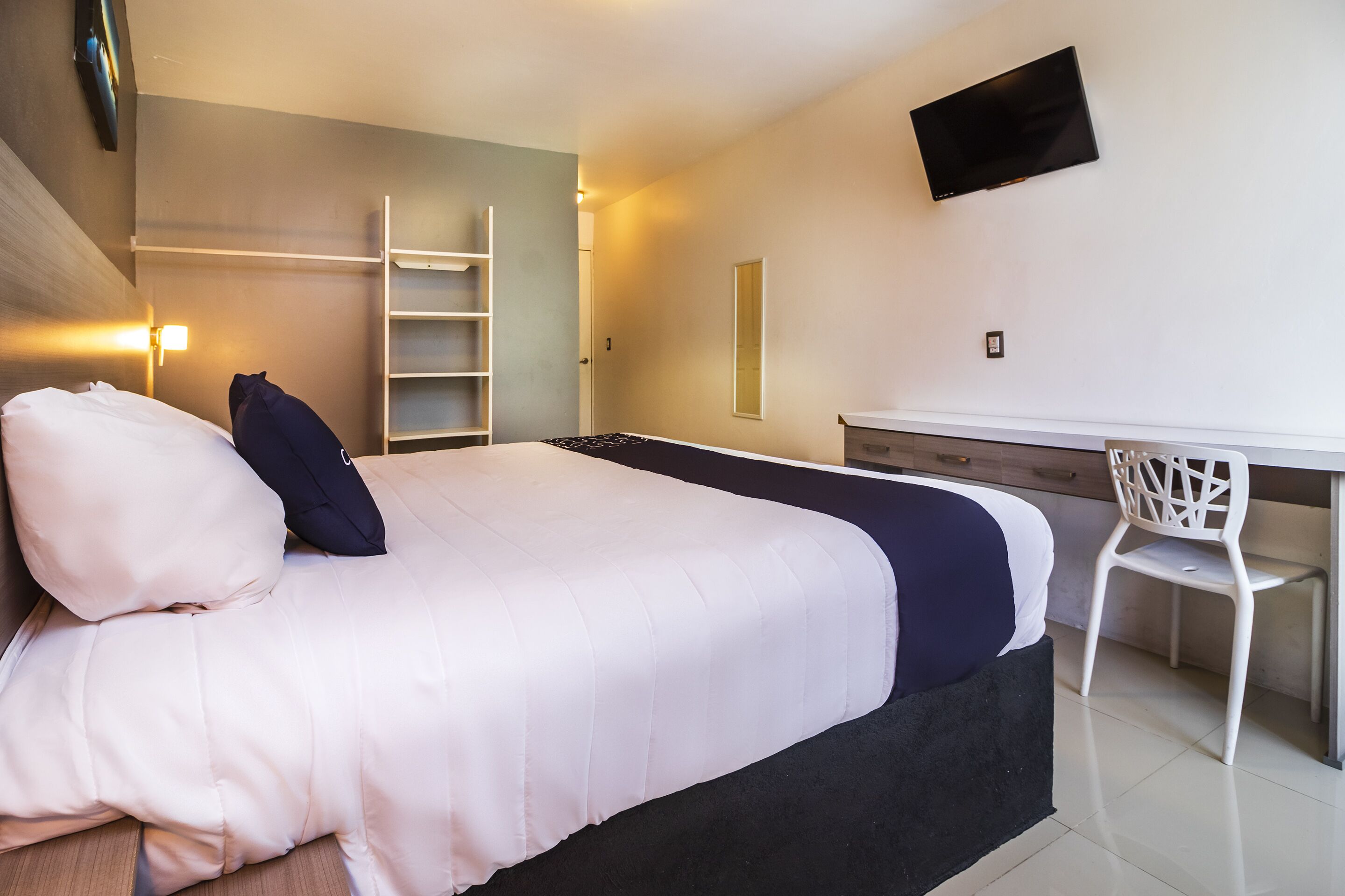 A bedroom with a bed, a desk, a chair, a TV, and a wardrobe.