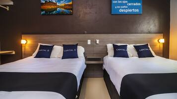 A hotel room with two beds, each with a white and black bedspread, and matching pillows. There are wall-mounted lamps on either side of the beds, and a painting above the beds.