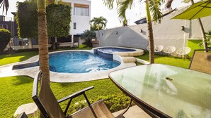 A modern outdoor pool area with two hot tubs, a glass table, and a seating area with chairs.