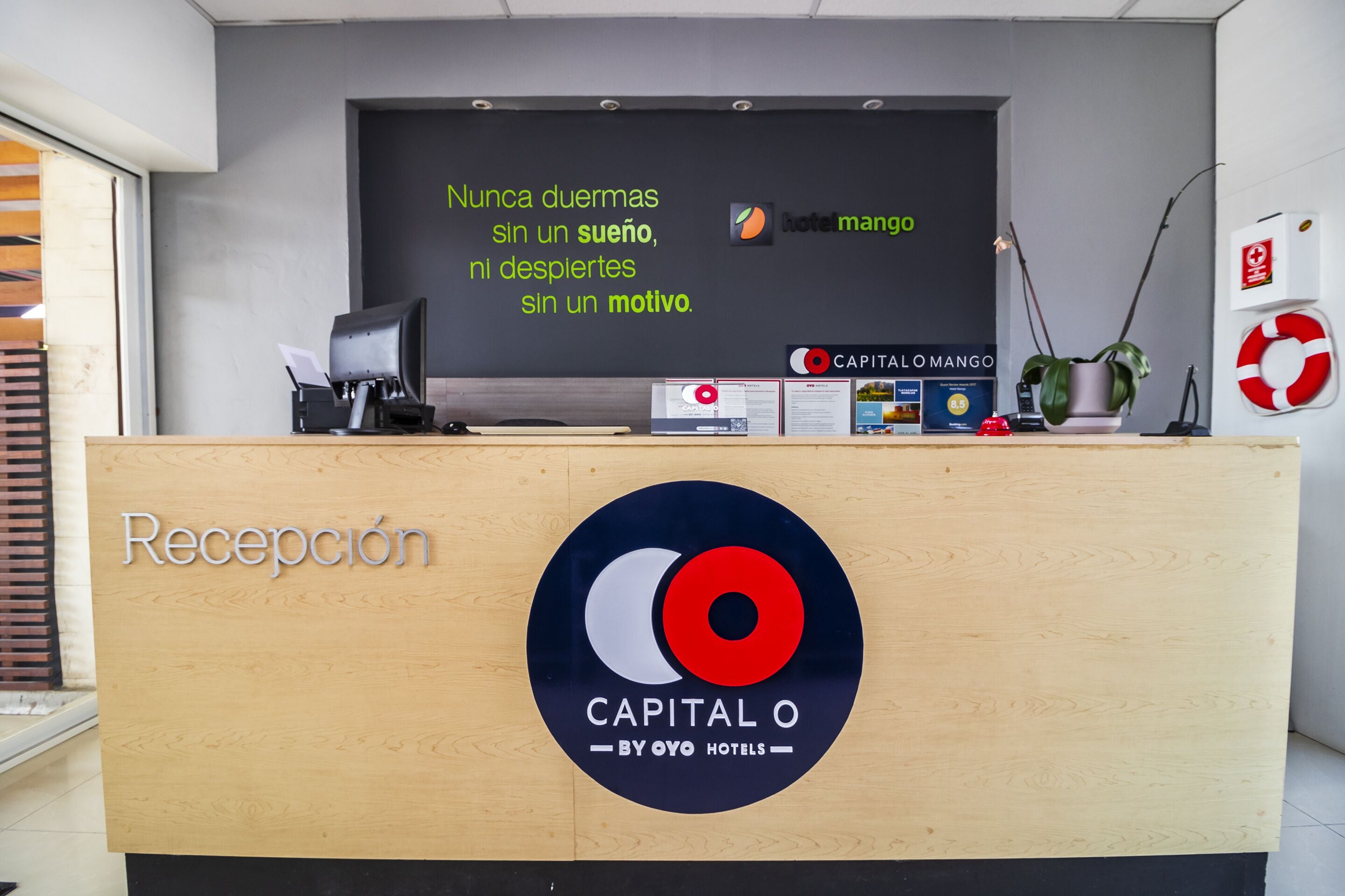 Un mostrador de recepción con un letrero que dice 'Recepción' y el logotipo de 'Capital O by Oyo Hotels'.