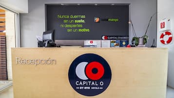 Un mostrador de recepción con un letrero que dice 'Recepción' y el logotipo de 'Capital O by Oyo Hotels'.