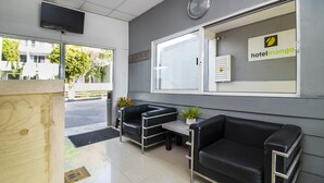 A hotel reception area with a reception desk, two black leather sofas, a clock, and a window with a sign reading "hotel mango".