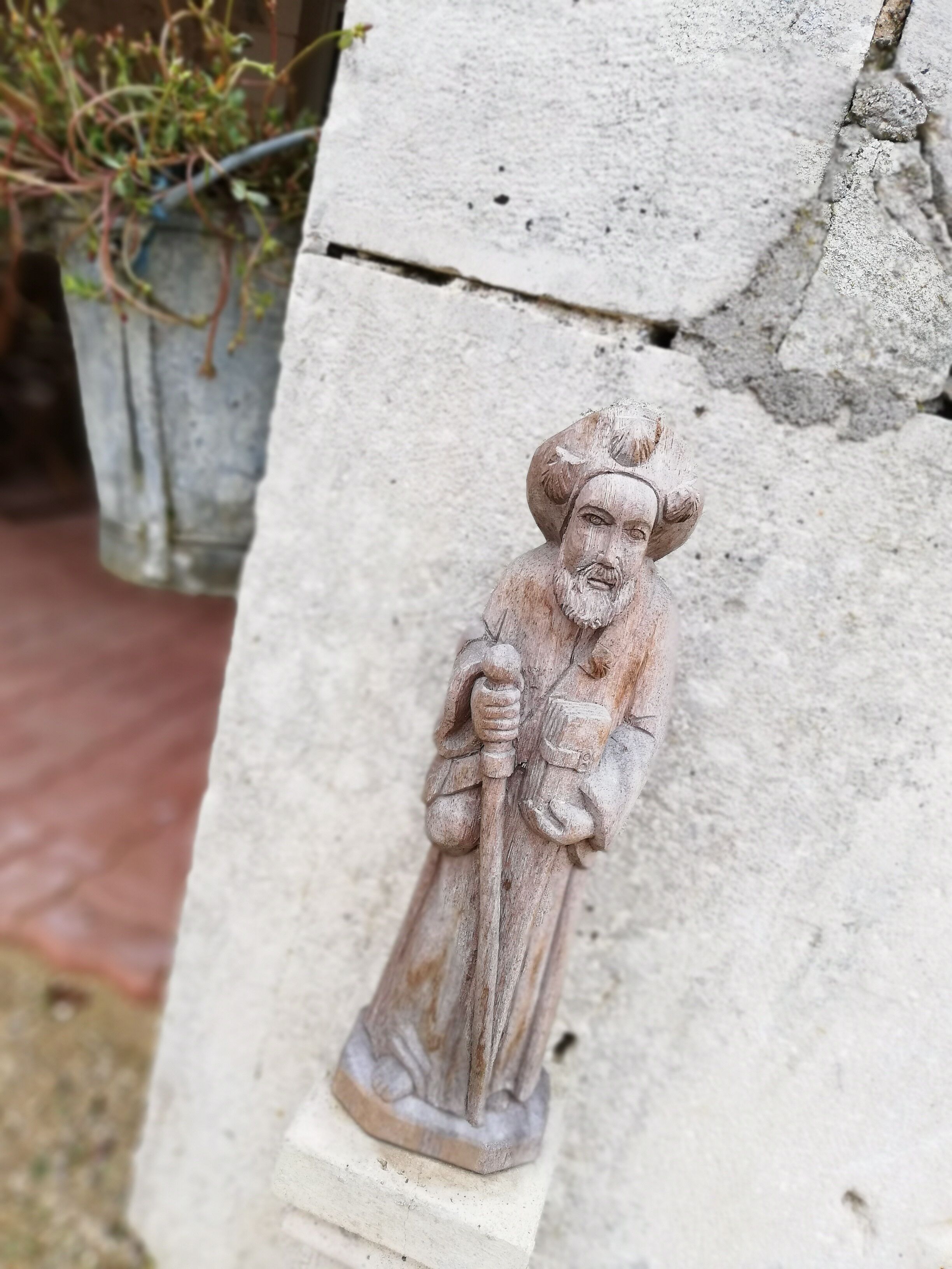 A stone statue of a figure holding a staff, mounted on a concrete structure.