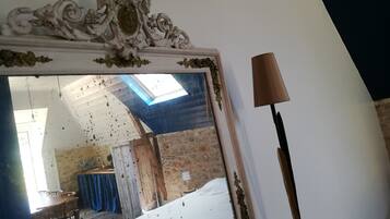 A room with a bed, a table, and a mirror reflecting a room with a blue ceiling and a window.