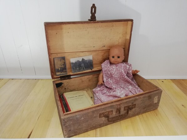 Une poupée ancienne, dans une boîte en bois dotée d’un couvercle à charnière, posée sur un plancher en bois.