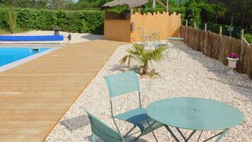 Une terrasse en bois avec une piscine, une petite construction en bois et un espace salon extérieur.