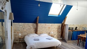 A bedroom with a large bed, a skylight, a wooden ceiling, a stone wall, and a small kitchenette. - Le Puits de Garival (Tour-de-Faure)