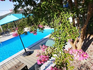 Una piscina con cubierta de madera, rodeada de follaje y flores rosadas.