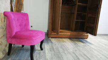 Una butaca rosa tapizada con patas negras en una habitación con suelo de madera y un armario de madera con puertas de vidrio.