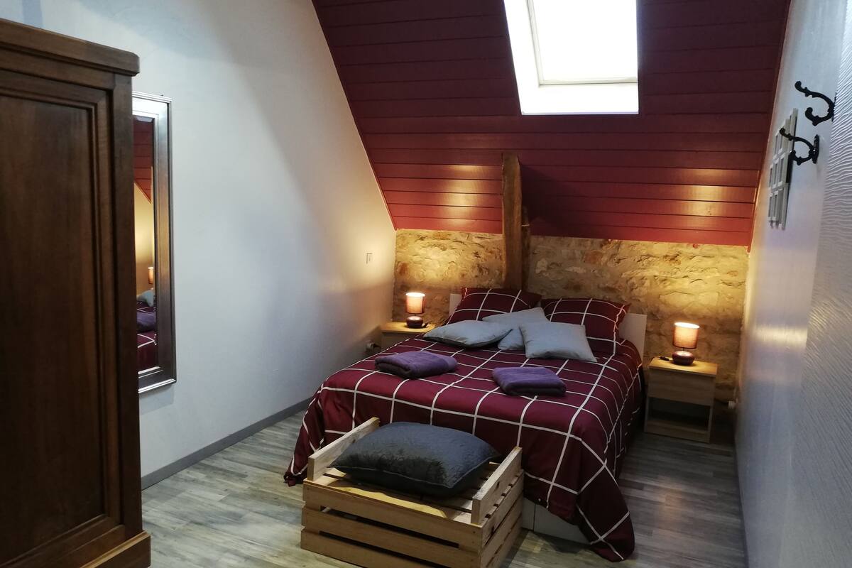 A bedroom with a sloped ceiling, a skylight, a wooden bed frame, a wooden nightstand, and a small wooden chest.
