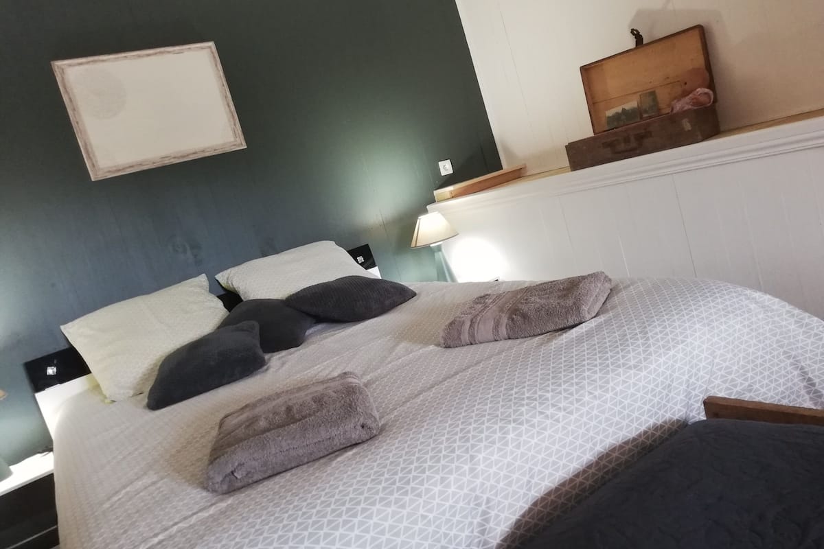 A bed with a patterned bedspread, multiple pillows, and a headboard against a dark wall.