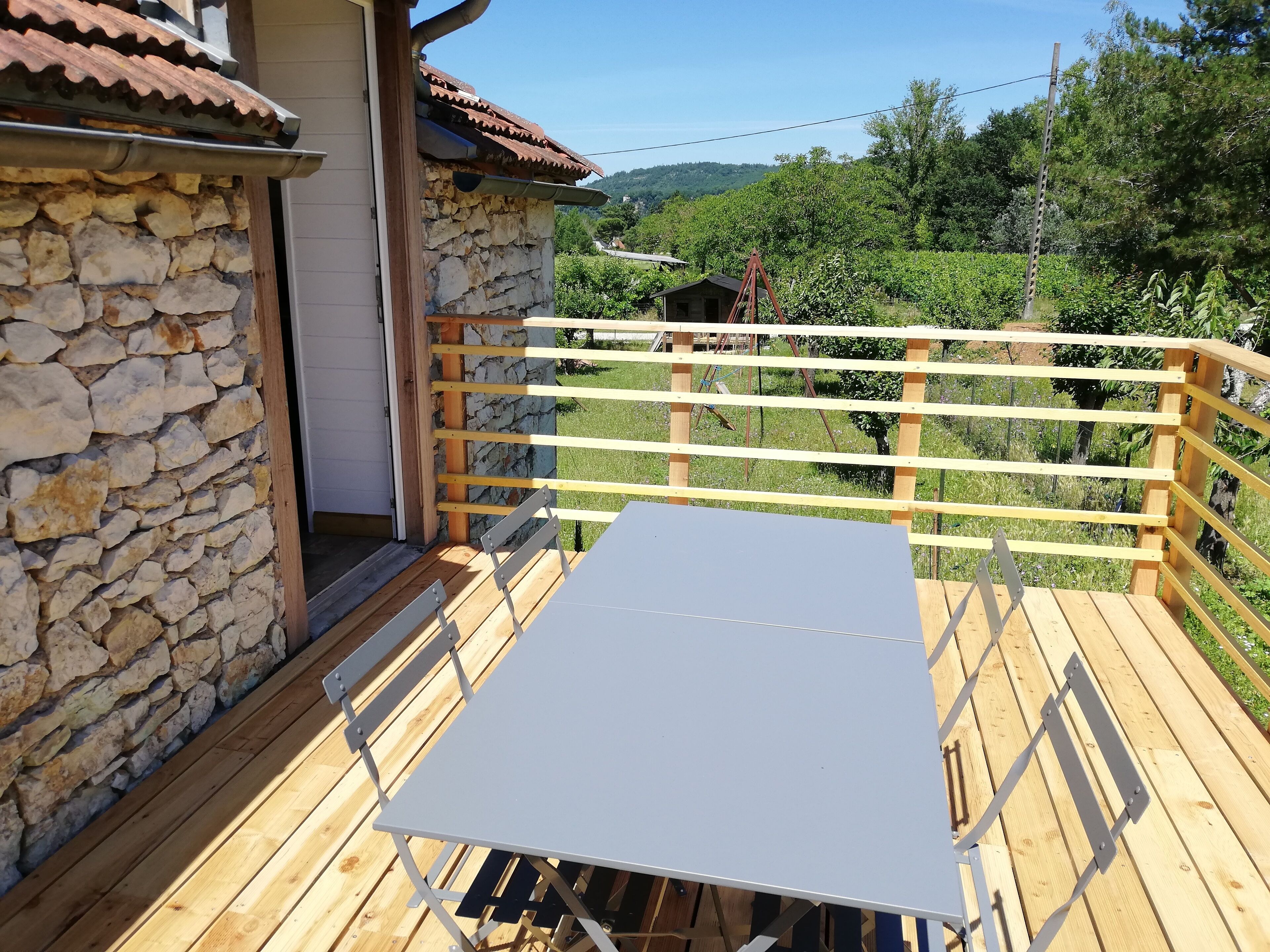 Une terrasse en bois avec une table et des chaises, des murs en pierre et une vue sur un paysage verdoyant.