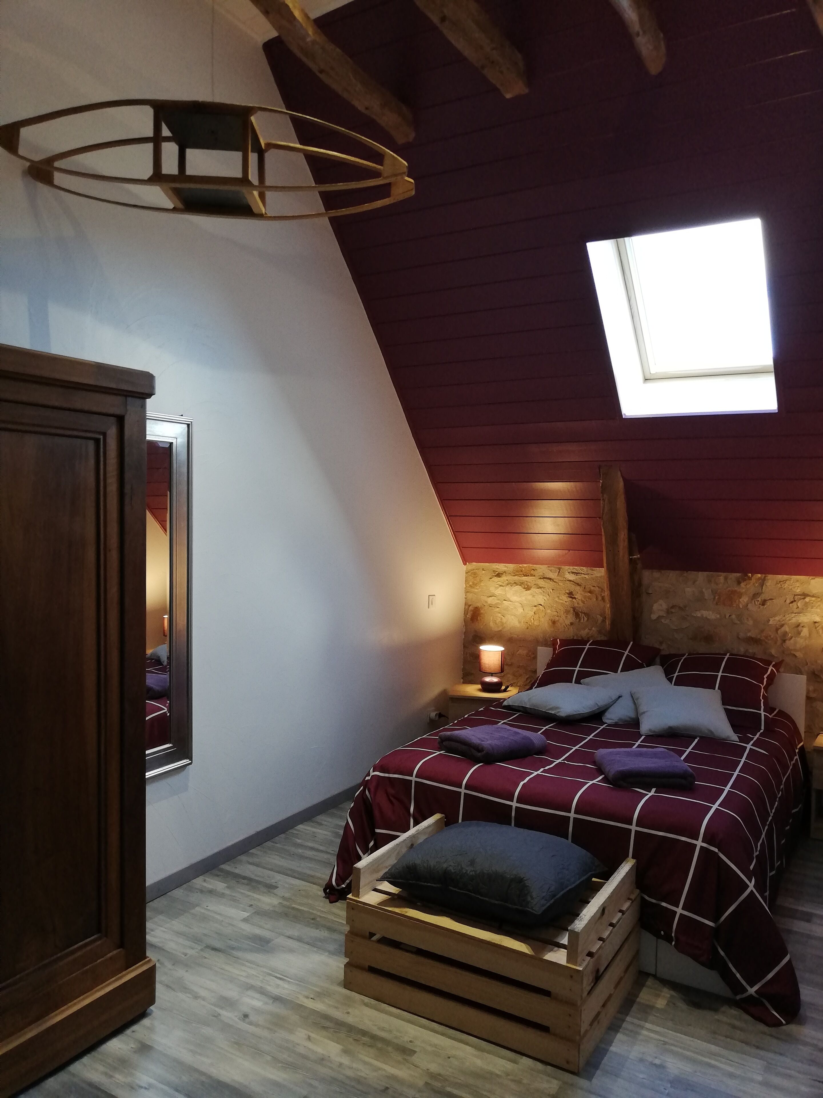 A bedroom with a sloped ceiling, a skylight, a wooden headboard, a bed with a checkered bedspread, and a nightstand with a lamp.