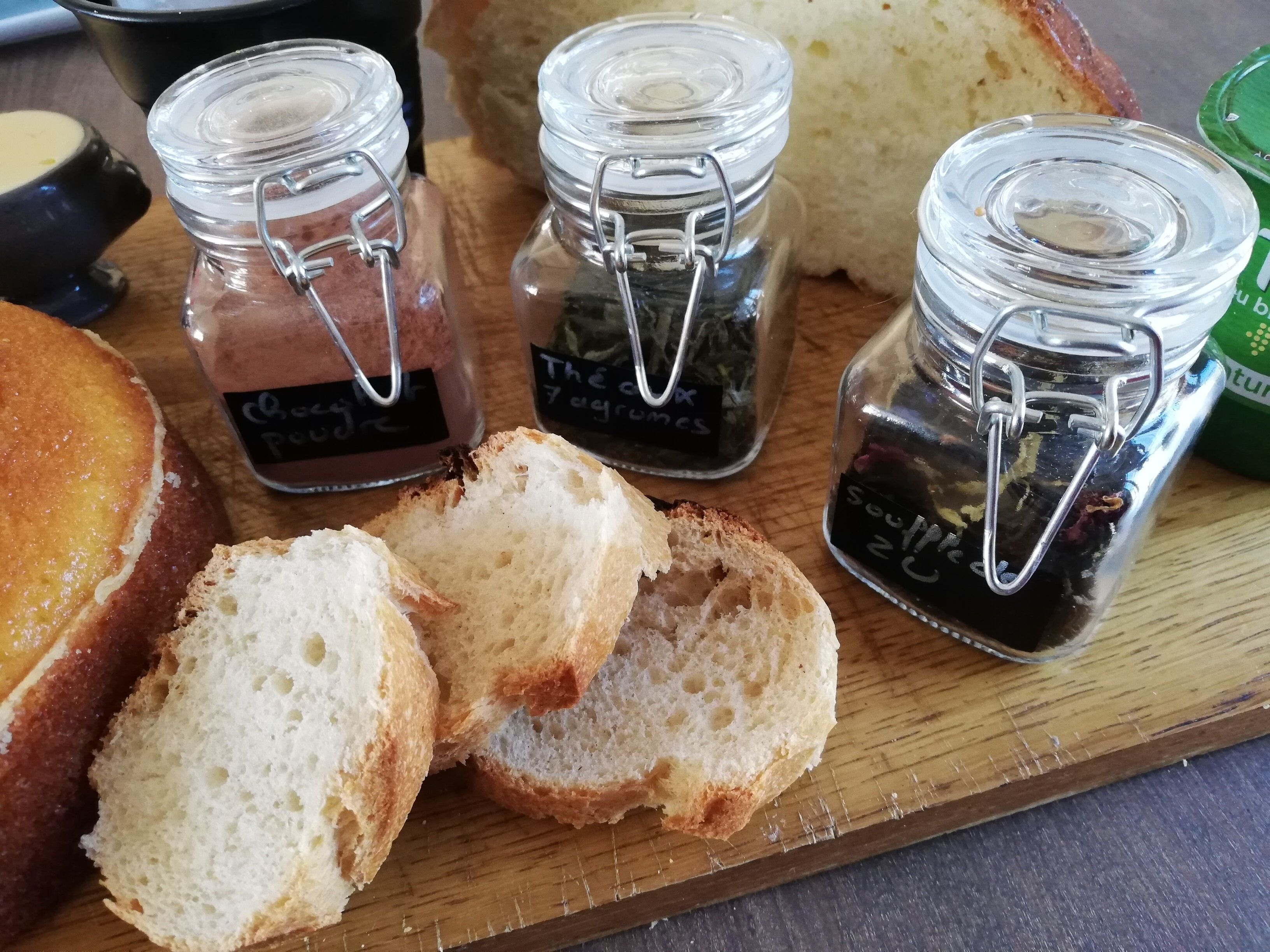 Una tabla de madera con pan rebanado, una hogaza de pan y dos frascos de vidrio con cierres metálicos.