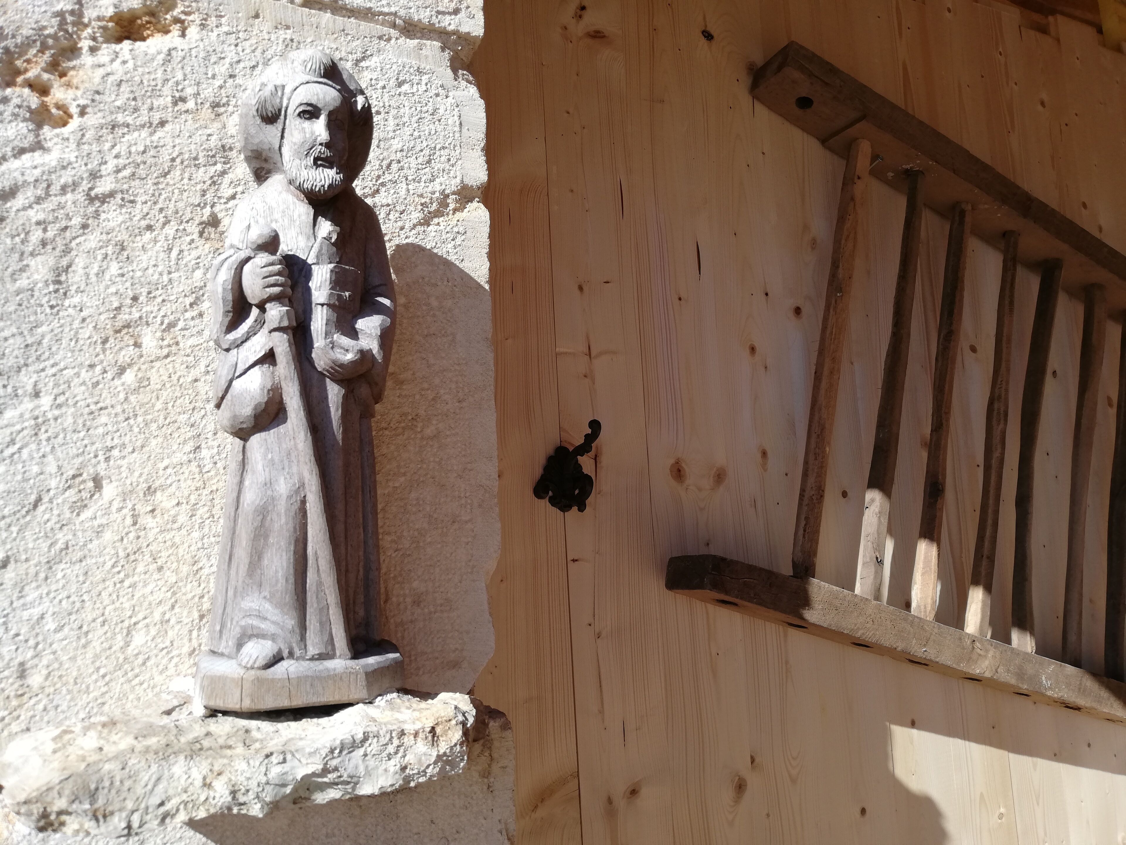 En trædør med et lille vindue og en stenhugget figur.