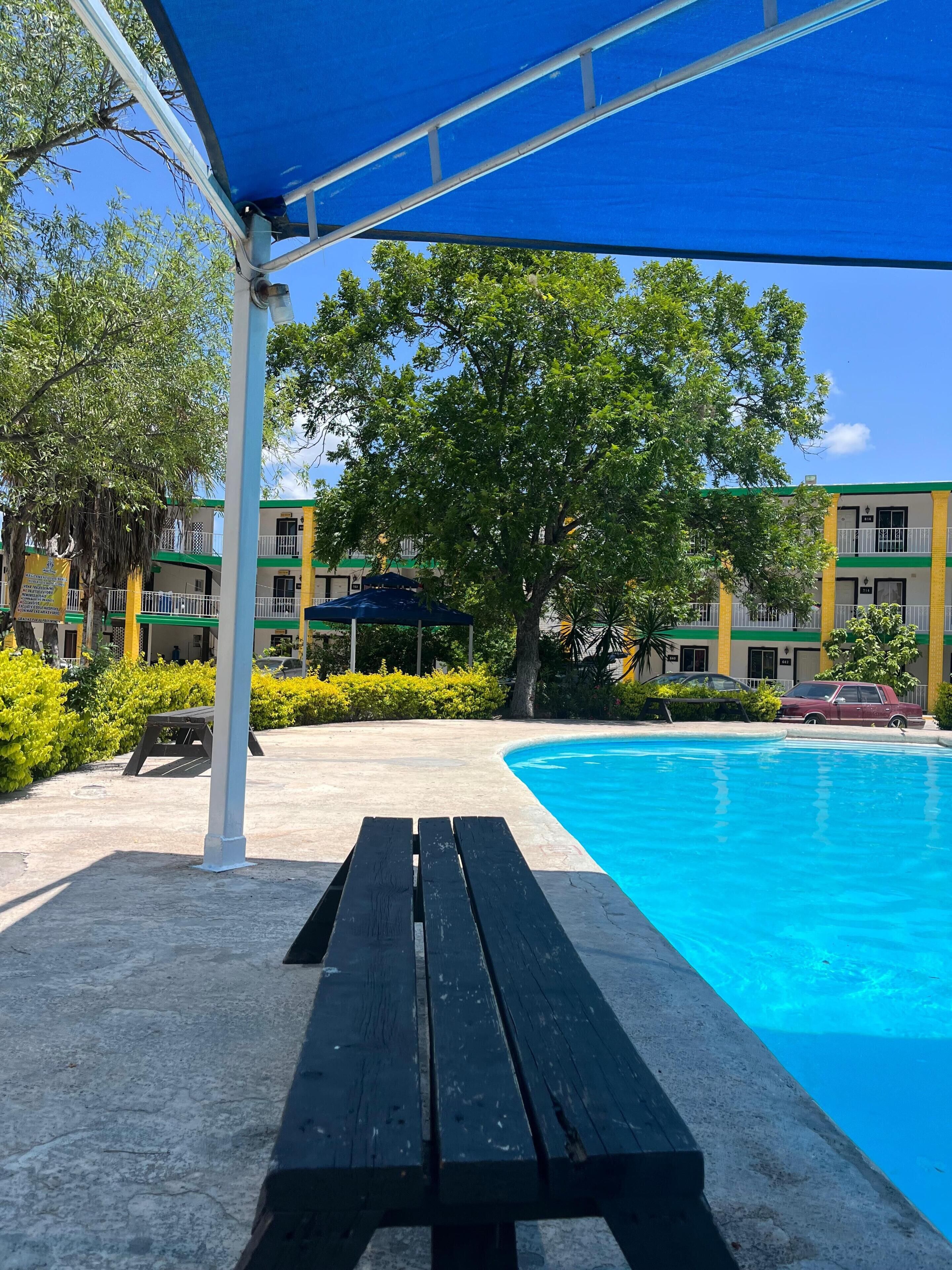 A swimming pool with a covered area, a bench, and a building with balconies in the background.