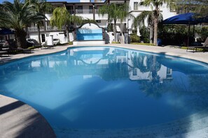 A clear swimming pool with lounge chairs and palm trees, surrounded by a multi-story building with balconies. - Hotel Virrey (Reynosa)