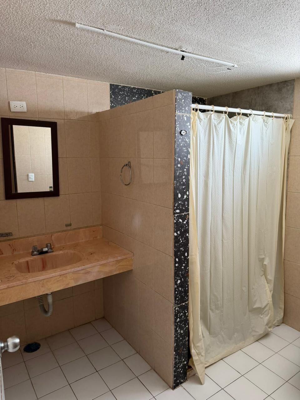A bathroom with a sink, mirror, shower curtain, and tiled floor.