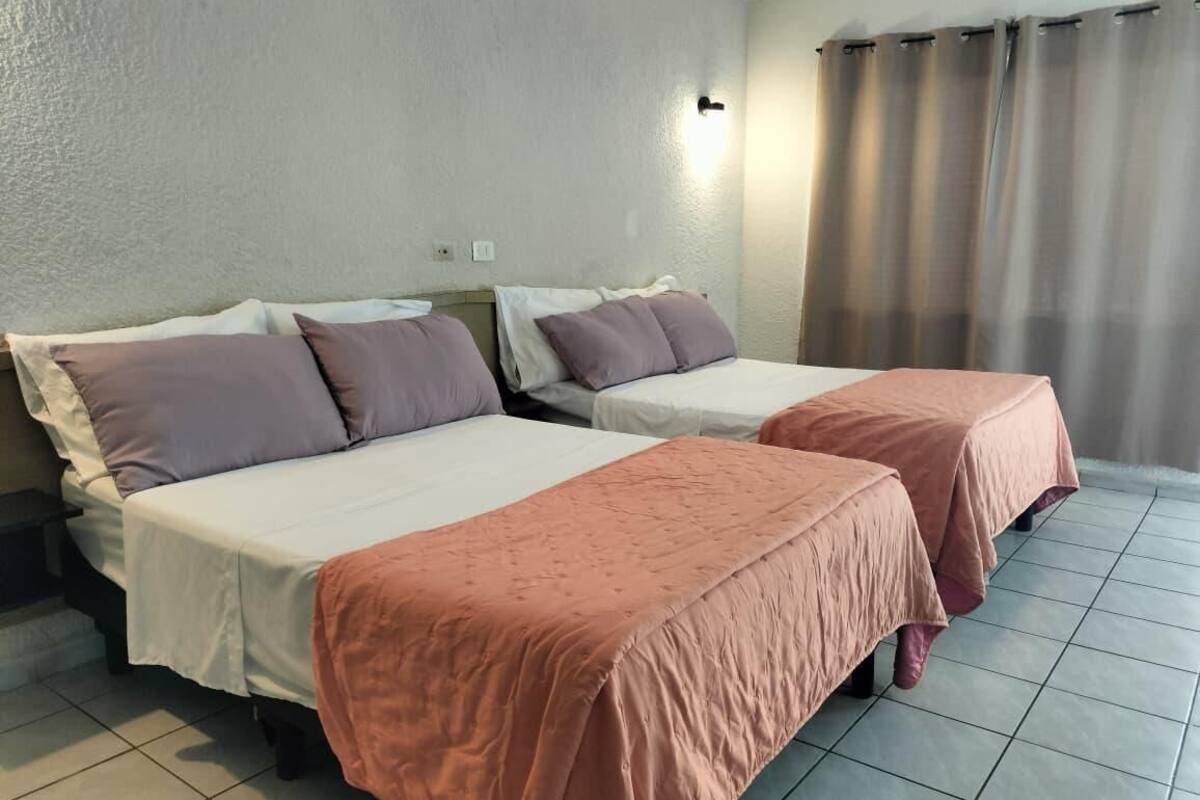 A hotel room with two beds, a nightstand, a wall-mounted light, and a curtain.