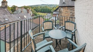 Ein Balkon mit Tisch und Stühlen, mit Blick auf ein Dorf mit traditionellen Steinbauten und einem Fluss.