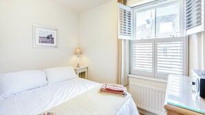 Ein Schlafzimmer mit Bett, Nachttisch mit Lampe, Heizkörper und Fenster mit Jalousien.