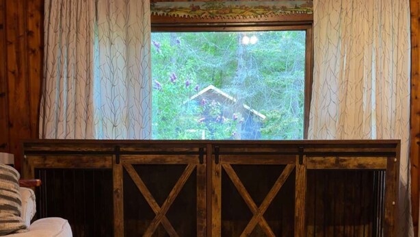 Een kamer met houten vloeren, een raam met gordijnen, een bank en uitzicht op groen.