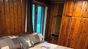 Een houten blokhut van binnen met een bed, een raam en een houten kast.
