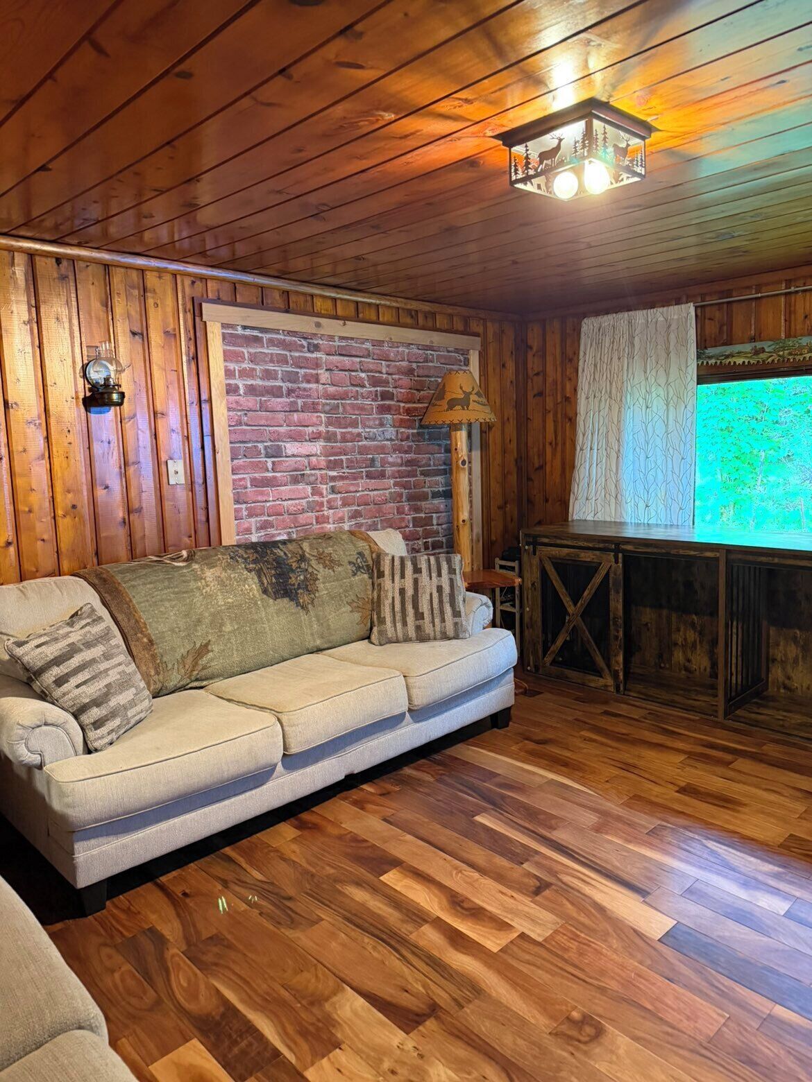 A cozy room with wooden walls, a brick accent wall, a wooden floor, a sofa, a lamp, and a table.