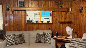 Een gezellig interieur van een blokhut, met een houten plafond, een bank met gestreepte kussens, een ventilator en een raam met uitzicht.