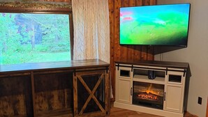 Een kamer met houten vloer, een aan de muur bevestigde televisie en een open haard.
