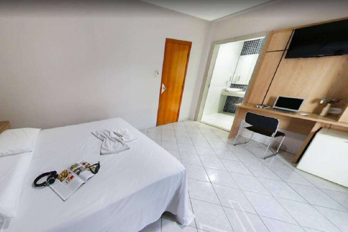 Una habitación de hotel con una cama, un escritorio con una computadora portátil, una silla y un televisor en la pared.