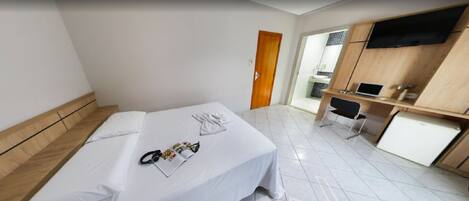 Une chambre d’hôtel avec un lit, un bureau avec un ordinateur portable, une chaise et un téléviseur fixé au mur.