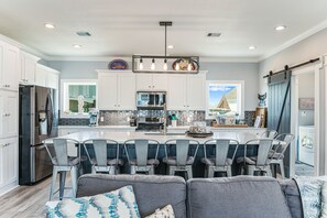Uma cozinha moderna com armários brancos, uma geladeira de aço inoxidável, uma ilha central com banquetas e um pendente.