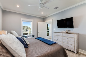 Um quarto com cama, cômoda, televisão e ventilador de teto.