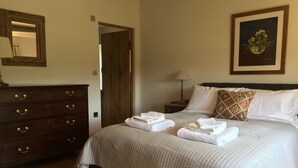 A neatly made bed with folded towels, a wooden dresser with brass handles, a framed picture on the wall, and a wooden door in the background. - A stylish Barn conversion with the perfect mix of industrial and country styling (Bradford-on-Avon)