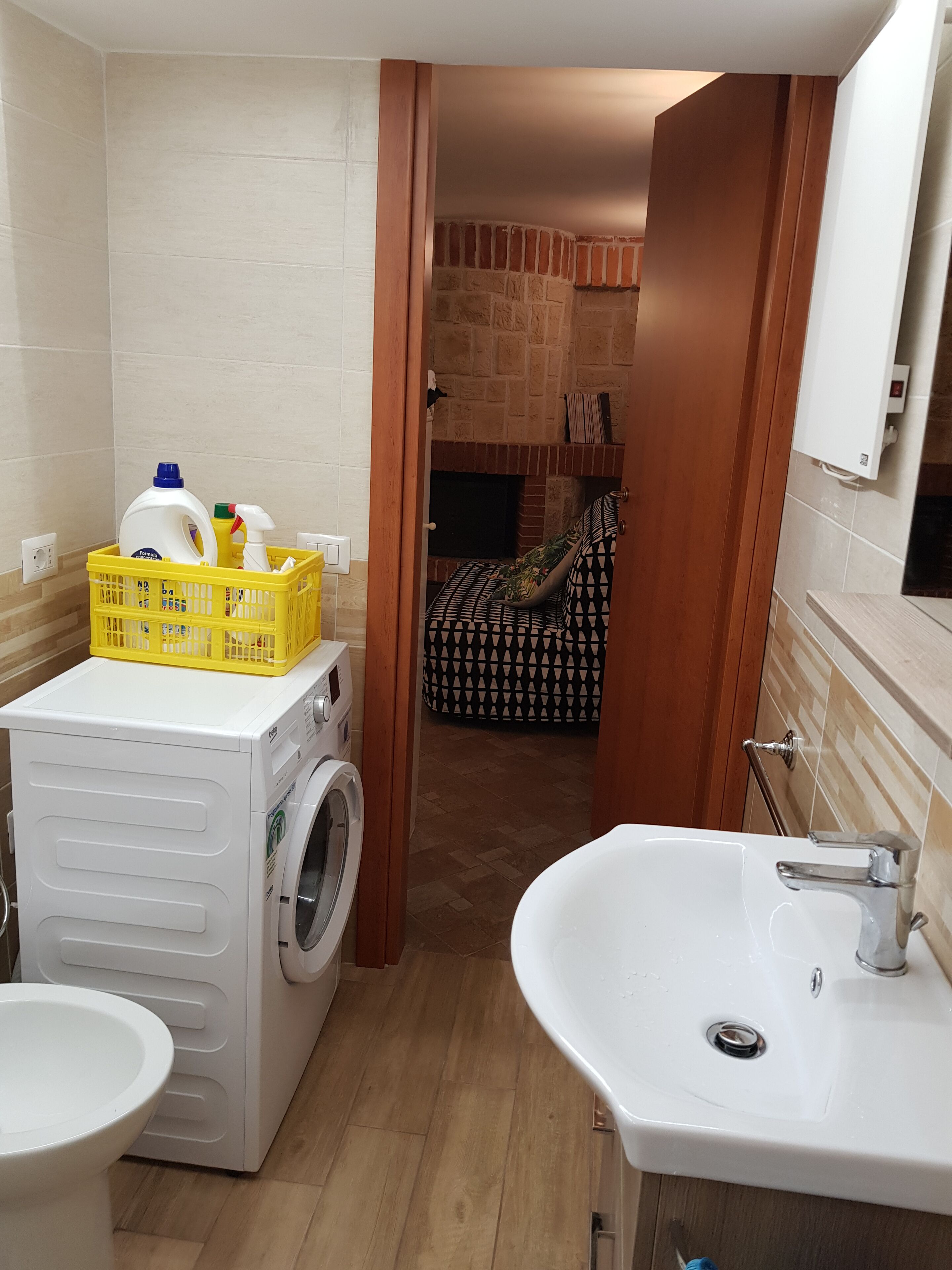 A compact bathroom with a washing machine, a sink, and a small storage basket.