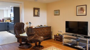 A living room with a leather chair, a wooden cabinet, a television, and a kitchen in the background. - The Annex at Fernyrig (Coldstream)