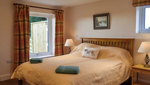 A bedroom with a large bed, two bedside lamps, a window with curtains, a framed picture on the wall, and a small rug on the floor. - The Annex at Fernyrig (Coldstream)