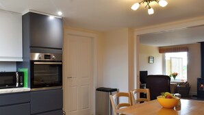 A modern kitchen with a built-in oven, microwave, and a dining area with wooden chairs and a table. - The Annex at Fernyrig (Coldstream)