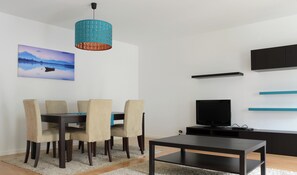 Uma sala de estar moderna com área de jantar, televisão de tela plana e uma pintura de um lago.