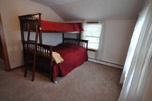 Une petite chambre avec un seul lit, un lit superposé, une fenêtre avec des rideaux et un sol recouvert de moquette.