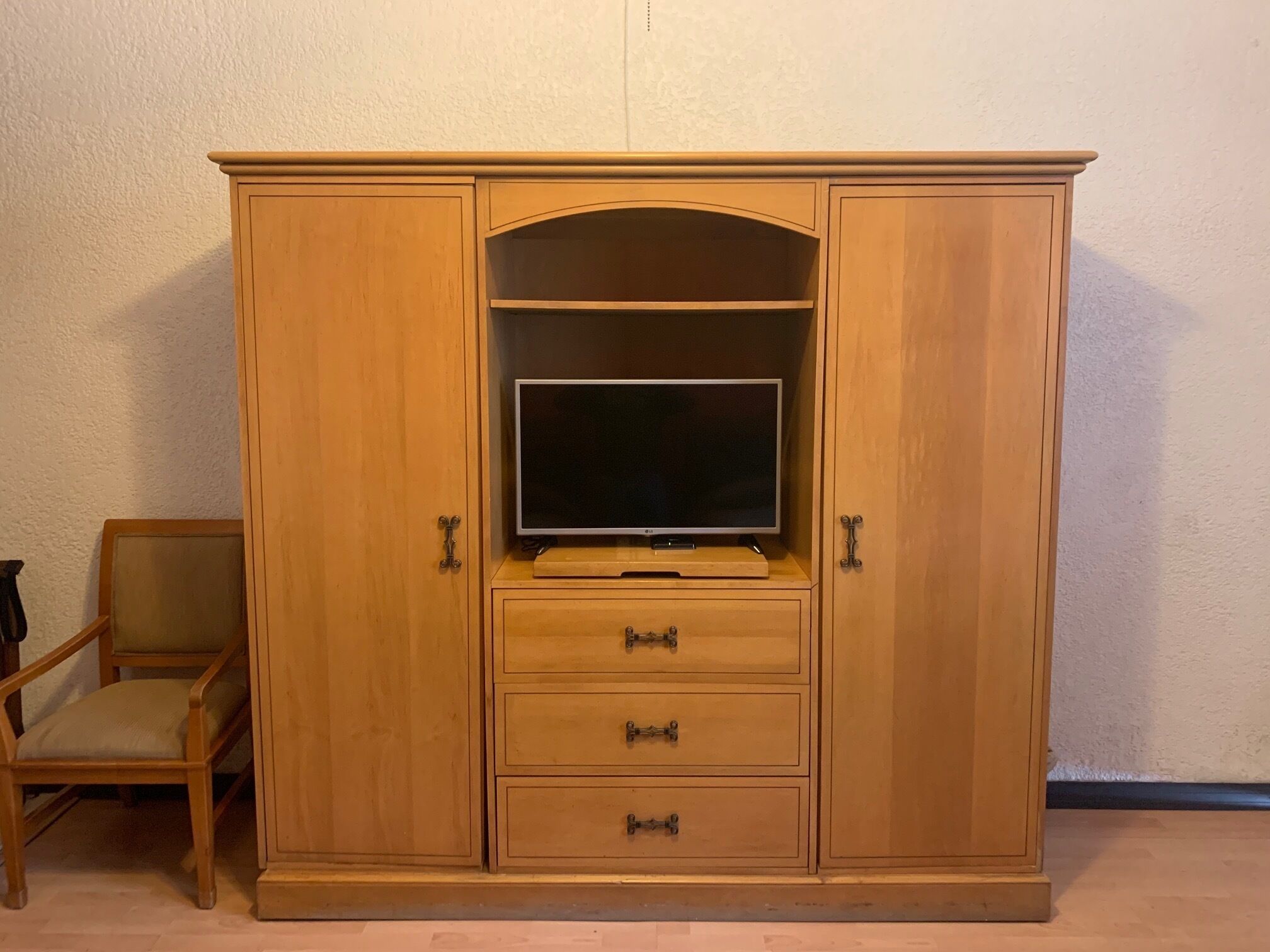 A wooden cabinet with a television on top, drawers, and a chair.