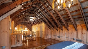 A spacious attic bedroom with wooden beams, a bed, a desk, and a dining area. - Rustic meets industrial: pet-friendly barn with  near Nashville, Indiana! (Nashville)