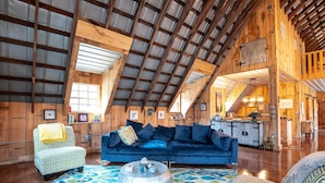 A spacious loft with high ceilings, exposed wooden beams, a blue sofa, patterned armchairs, and a dining area. - Rustic meets industrial: pet-friendly barn with  near Nashville, Indiana! (Nashville)